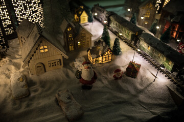 Naklejka premium Miniature of winter scene with Christmas houses, train station, trees, covered in snow. Nights scene. New year or Christmas concept.