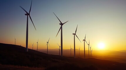 Obraz premium Scenic view of a wind farm at sunset, with large wind turbines silhouetted against a colorful sky. Rolling hills and green fields highlight the harmony between technology and nature.