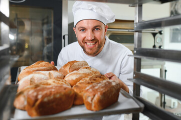 Male baker holding a tray of baked breads in bakery shop