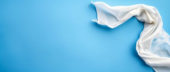  A tight shot of a white fabric against a blue backdrop, featuring a solitary milk drop in the frame's center