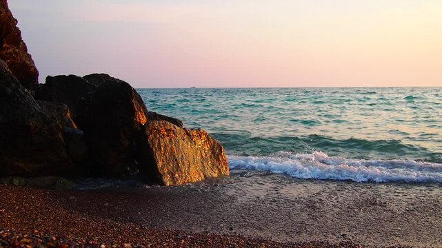 Waves gently lap at shore during stunning sunset over ocean. Golden sunlight reflects off waves as they roll onto shore, creating tranquil atmosphere at sunset by sea. Montenegro summer Canj