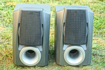 pair of big square powerful plastic gray old electric acoustic music dirty industrial speakers standing on green grass during daytime outdoors