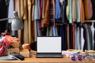 Background shot of laptop with blank white screen on table cluttered with thrift store items and...