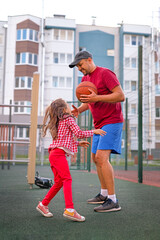 Dad teaches his little daughter to play basketball in the backyard. The child likes to spend time...