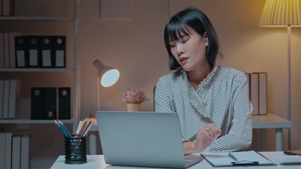 Asian office worker struggles with a stomach ache while working late at night, showcasing the challenges of overwork