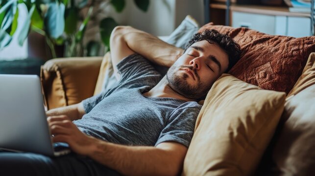 A young Middle-Eastern male relaxes on a couch, peacefully sleeping with a laptop beside him.