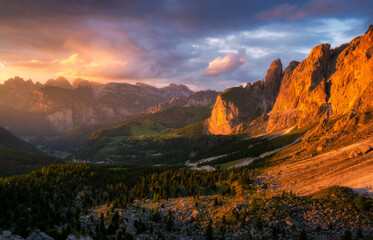 Mountains at beautiful golden sunset in summer. Dolomites, Italy. Colorful landscape with mountain peaks, rocks, alpine meadows, stones, trees, green grass, orange sunlight, vibrant sky with clouds