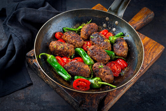 Traditional Croatian cevapi spicy meat ball rolls with tomatoes and paprika served as close-up in a rustic skillet