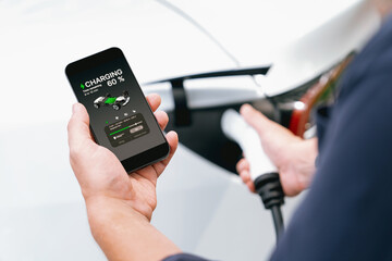 Man using smartphone online banking application to pay for electric car battery charging from EV...