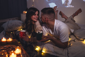 Romantic evening, cozy atmosphere, Christmas at home. Young attractive happy couple celebrating holidays, watching movies, drinking hot chocolate with marshmallow. Lazy weekend concept