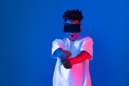 Young African American player wearing VR playing sword or baseball hologram isolated blue pink neon lighting wall connecting digital futuristic technology virtual reality metaverse world. Contrivance.