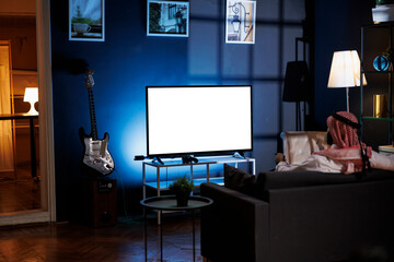 Back-view shot of Muslim guy in traditional attire seated on sofa in front of television displaying isolated white screen. Image showing man looking at tv screen with blank copyspace mockup template.