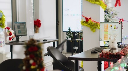 Empty festive ornate office properly decorated for company Christmas festivities. Accounting figures on computer screens in xmas adorn workplace with no workers during winter holiday season