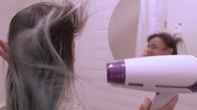 Dry your hair with a hairdryer. Rear view of the reflection in the mirror of a bny girl with a hair dryer.