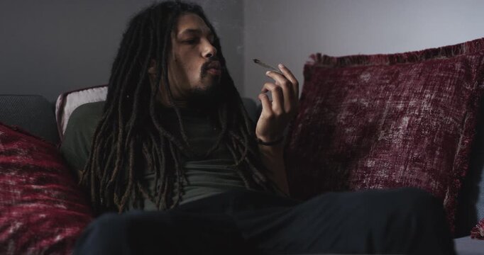 Man, cannabis and smoking cigarette in home living room on sofa to relax or 420. African person with marijuana weed, medical drugs abuse problem and hemp paper, natural cbd joint and thc addiction