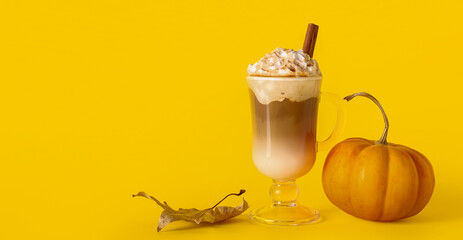 Glass cup of tasty pumpkin latte with cinnamon on yellow background