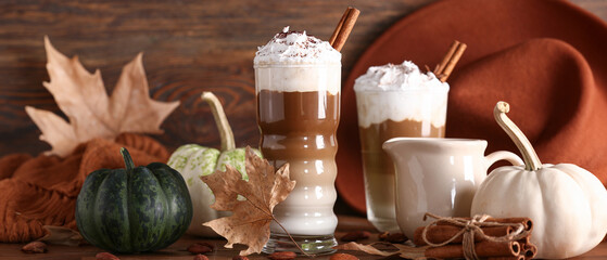 Glasses of tasty pumpkin latte with cinnamon and almond on wooden background