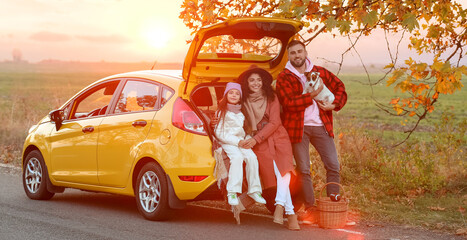 Parents with little daughter and cute dog sitting in car trunk