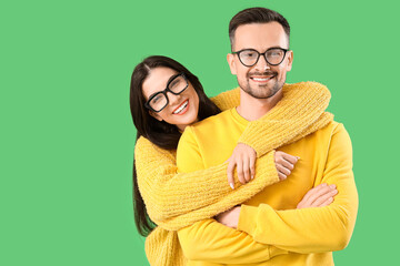 Young couple in eyeglasses hugging on green background