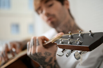 Cool tattooed young man playing guitar at home, closeup