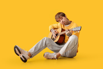 Cool tattooed young man playing guitar on yellow background
