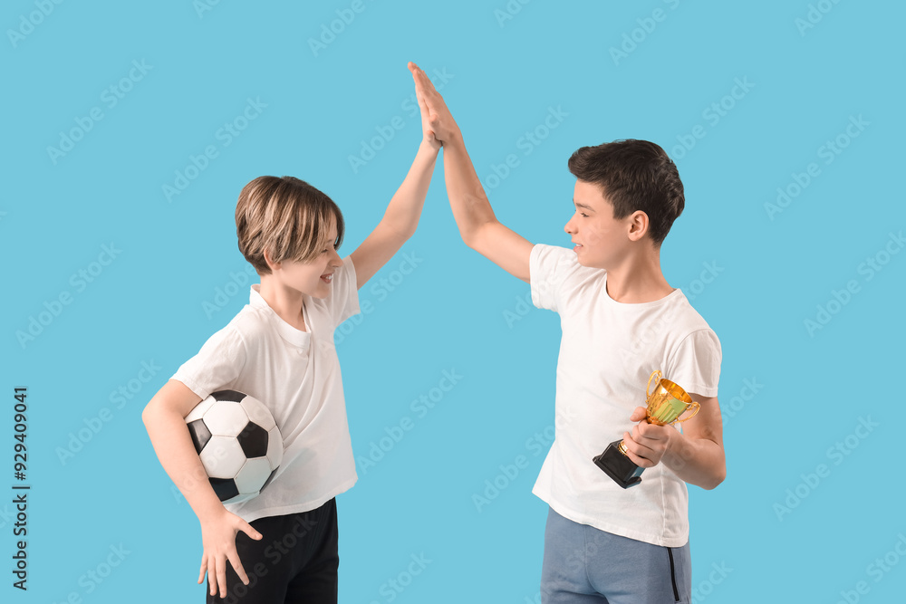 Poster happy brothers with soccer ball and gold cup giving each other high-five on blue background