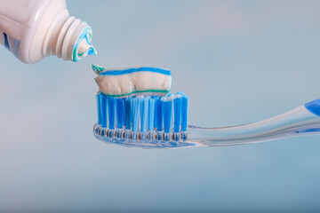 Toothbrush and toothpaste, Squeezing toothpaste onto toothbrush. Applying toothpaste on brush against blurred background, closeup.