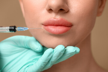 Young woman receiving filler injection in lips on brown background, closeup