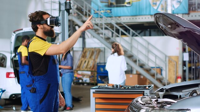 Mechanic in auto repair shop using virtual reality goggles to visualize car components in order to fix them. Repairman wearing futuristic vr headset while working on damaged vehicle
