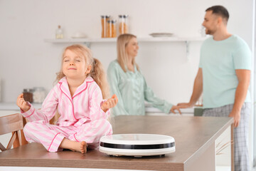 Fototapeta premium Little girl with robot vacuum cleaner meditating on table in kitchen