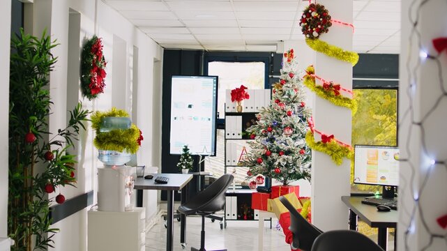 Tilt up shot of empty festive ornate modern office workspace with beautiful Christmas tree and lights. Xmas adorn workplace ready for festivities before winter holiday season vacation