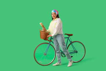 Young Asian woman with doner kebab and bicycle on green background