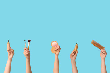 Female hands with highlighter, foundation, wooden comb, bottle of serum and brushes on blue background