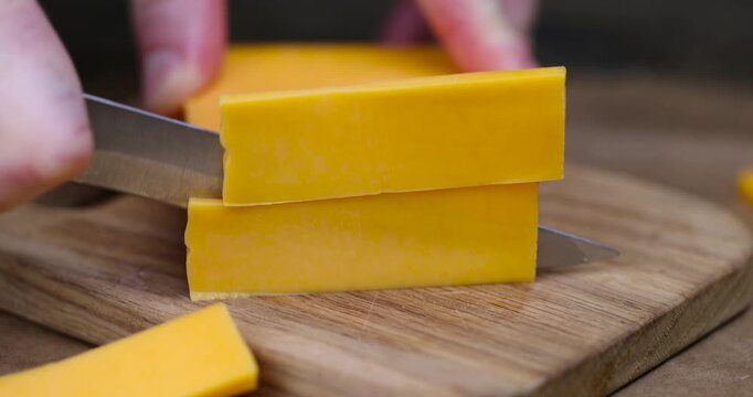 yellow hard cheese cut into long pieces, slicing yellow cheese close-up