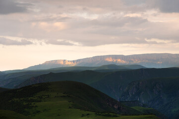 Beautiful picturesque sunset sky over green field in high mountains in the distance