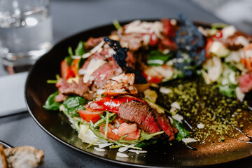 Beef salad with arugula and tomatoes on a black plate.