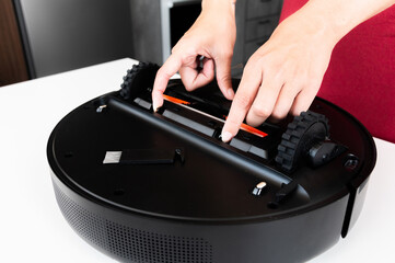 The hands of a Caucasian young woman are cleaned by a robot vacuum cleaner. An overturned vacuum cleaner on the table. Service