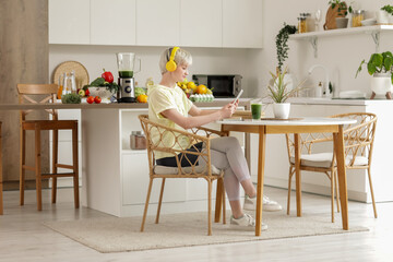 Sporty young woman with tablet computer and healthy smoothie in kitchen
