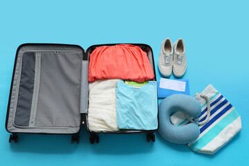 Travel pillow, wallet, ticket and suitcase with clothes on blue background