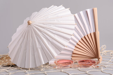 Mini umbrella with fan and sunglasses on grey background