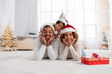 african american family in santa hat hugging at home for christmas and looking at camera, teenage boy celebrating new year with mom and dad and decorating house