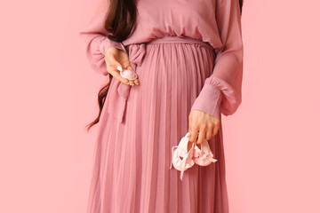 Young pregnant woman with baby pacifier and booties on pink background