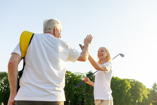 elderly senior couple in uniform celebrating victory and success in golf game and giving high five, old man and woman playing golf on golf course at sunset and doing outdoor sports