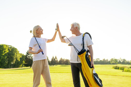 elderly senior couple in uniform celebrating victory and success in golf game and giving high five, old man and woman playing golf on golf course at sunset and doing outdoor sports