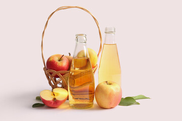 Bottles of fresh apple cider and wicker basket with fruits on light background
