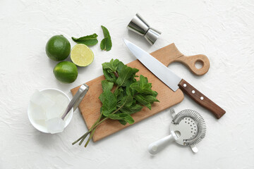 Wooden cutting board, knife and ingredients for preparing mojito on white background