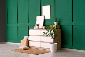 White dresser with photo frames and houseplants near green wall in living room