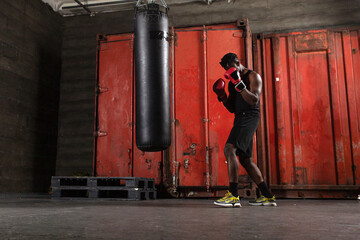 Powerful African American boxer wearing red gloves prepares to hit punching bag in gym showing his...