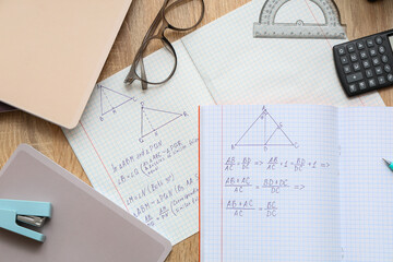 Copybooks with math formulas, eyeglasses and stationery on wooden background, closeup