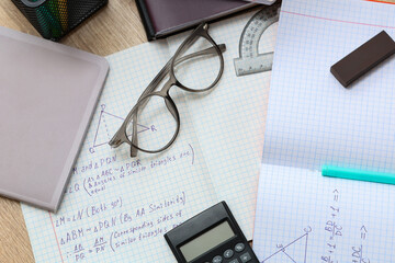 Copybooks with math formulas, eyeglasses and stationery on wooden table, closeup